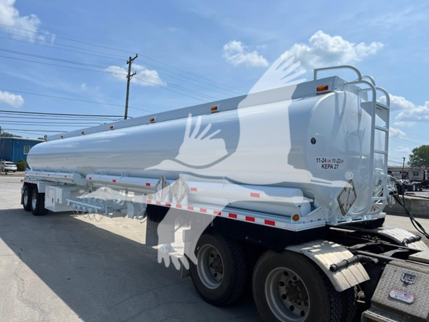 Tank trailer showing a white Heil petroleum tanker with dual rear wheels and a ladder at the back, side labeling visible, and compliance reflective tape along the sides.