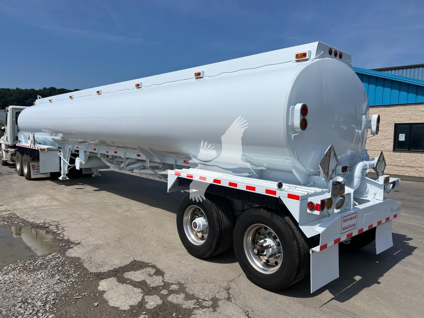 Heil tank trailer showing cylindrical tank and dual rear axles with white reflective striping and lights.