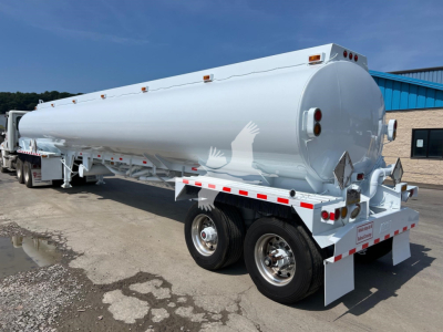 Heil tank trailer showing cylindrical tank and dual rear axles with white reflective striping and lights.