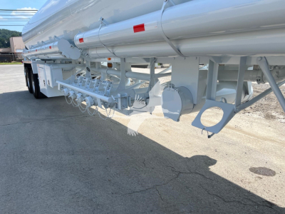Equipment trailer underside with multiple hanging hooks and structural supports, white paint, cylindrical tank visible.