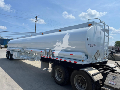 Tank trailer showing large cylindrical tank with white color, dual rear axles, and ladder. Side logo of a bird, safety decals, and rear end with mounted hoses and piping.
