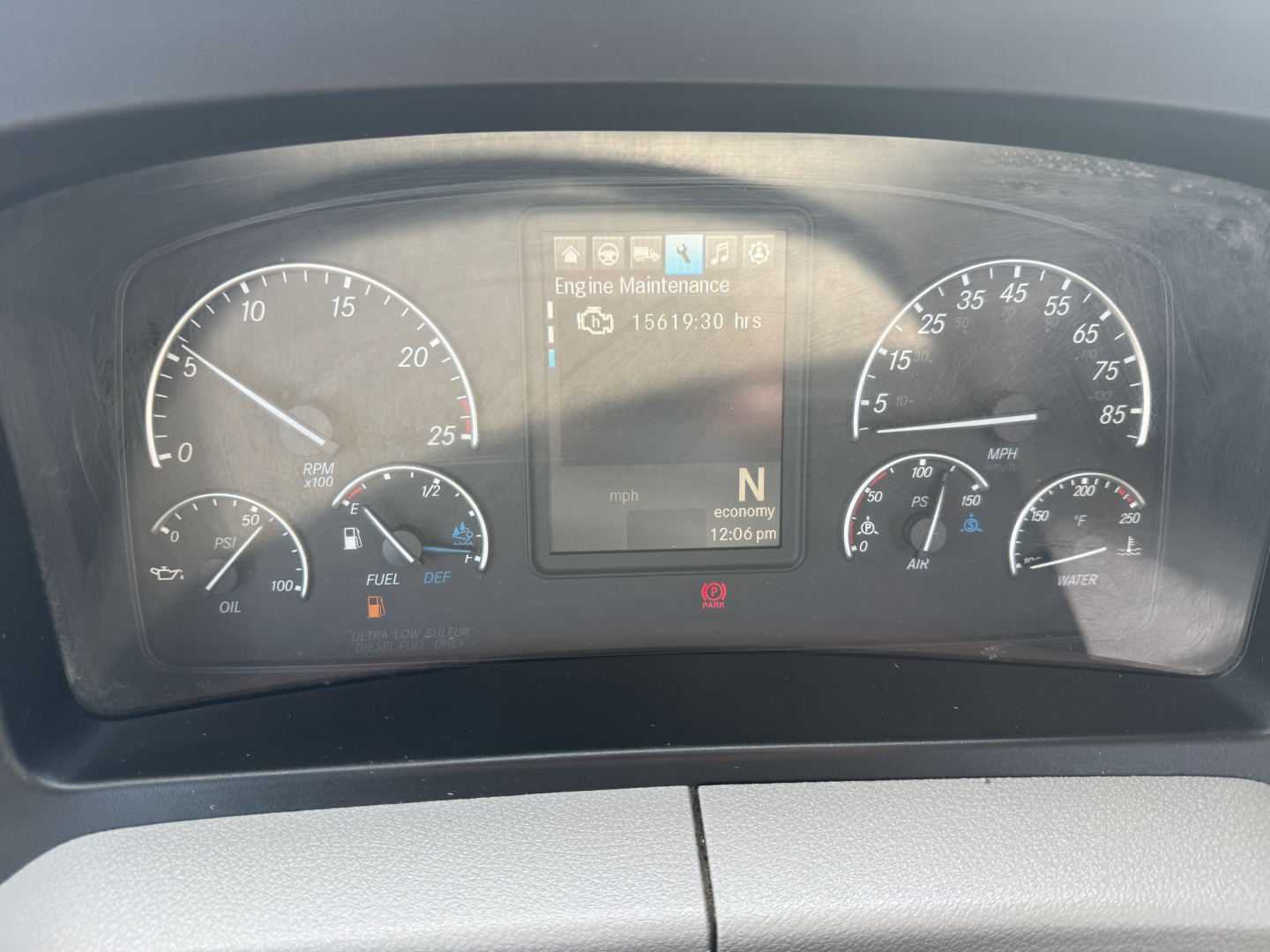 Dashboard of a Freightliner truck showing instrument cluster with speedometer, tachometer, fuel gauge, and central display reading Engine Maintenance 15619.30 hrs and N economy 12:06 pm.