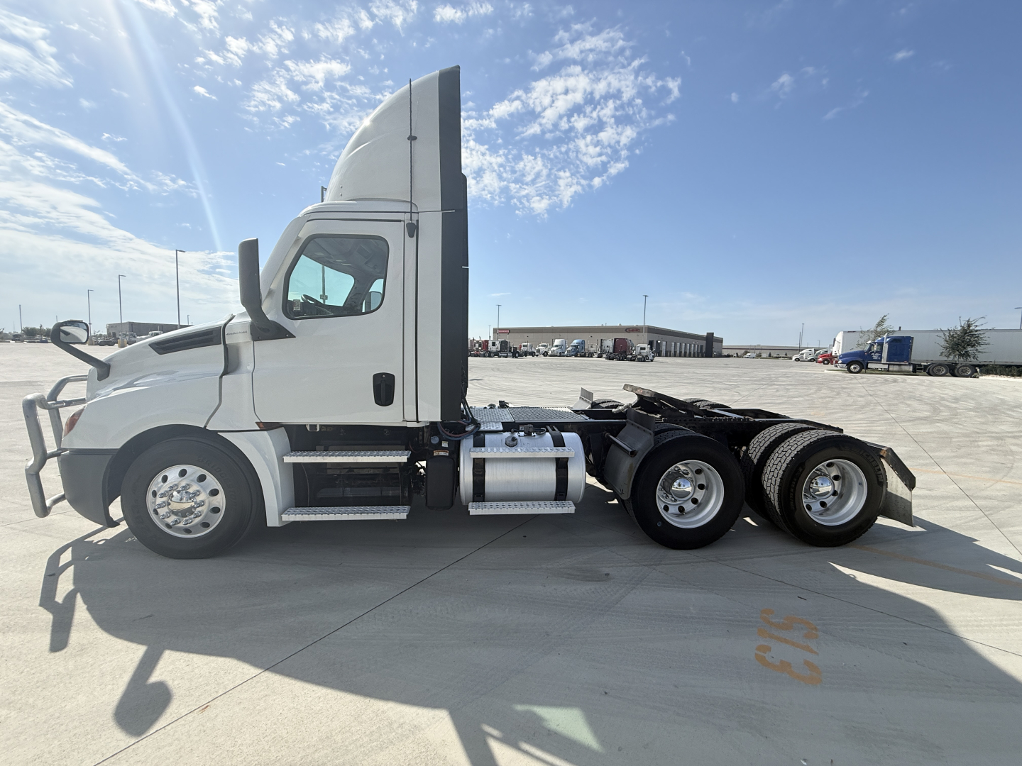 Truck side view showing Freightliner semi tractor with mid-height sleeper, two rear axles, white cab, fuel tanks, and tandem drive wheels.