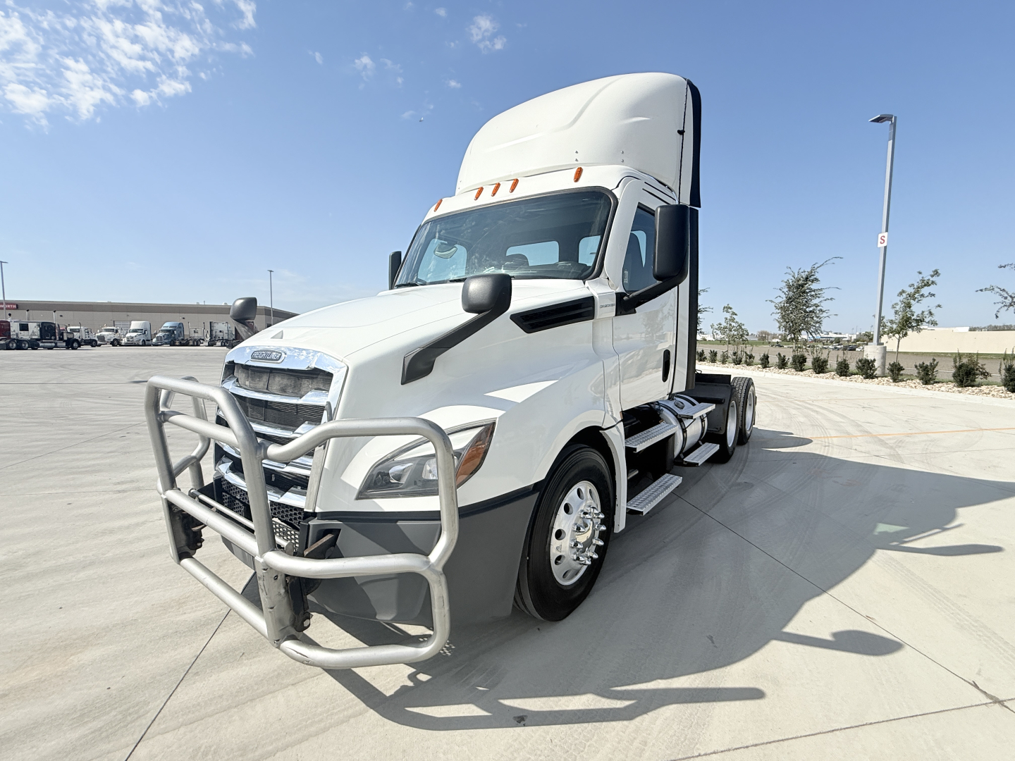 Front-right view of a white Freightliner semi-truck tractor with a grille guard. Cab shows side mirrors, aerodynamic hood, and sleeper. No visible text legible on decals or labels.