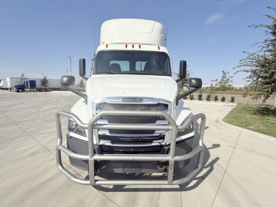 Truck front grille with bull bar bumper on a white Freightliner cab, large side mirrors, headlights, windshield, and hood badge visible.