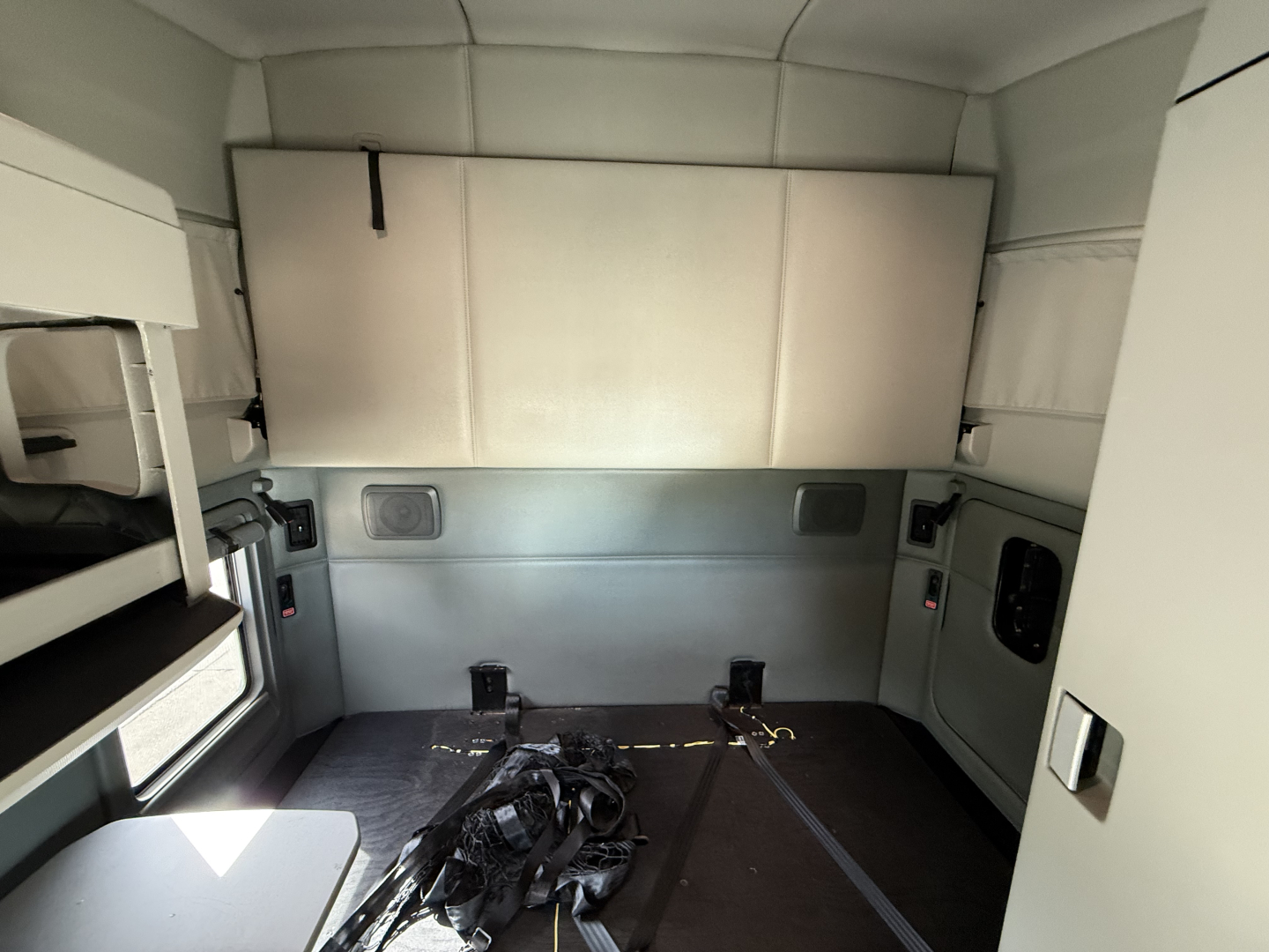 Kenworth T680 sleeper cab interior cargo area with dual overhead bunk, storage cabinet, and seat belts visible in the rear with metallic panels.