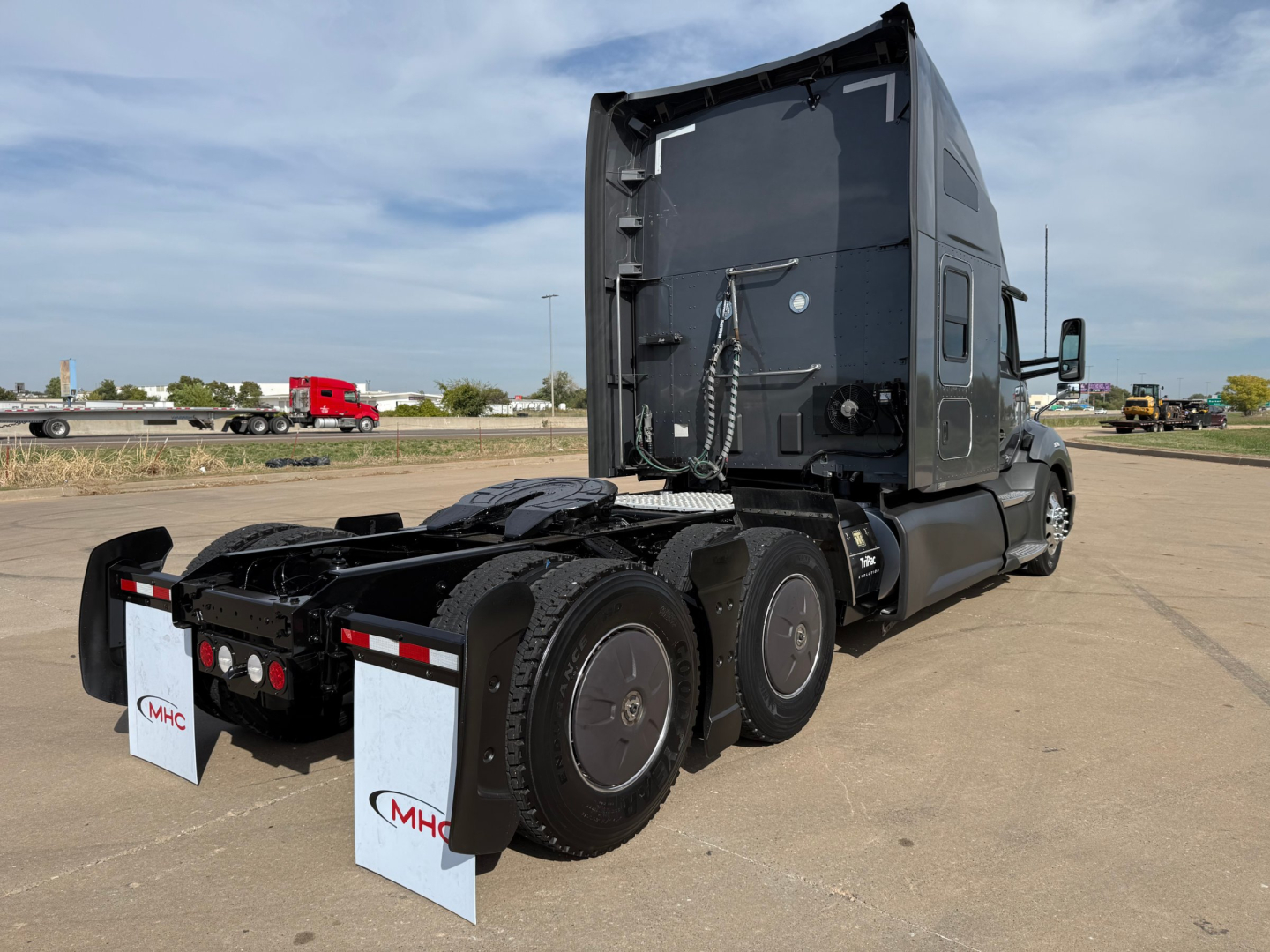 Kenworth T680 tractor rear view showing mud flaps and drivetrain with three axles and fifth wheel.
