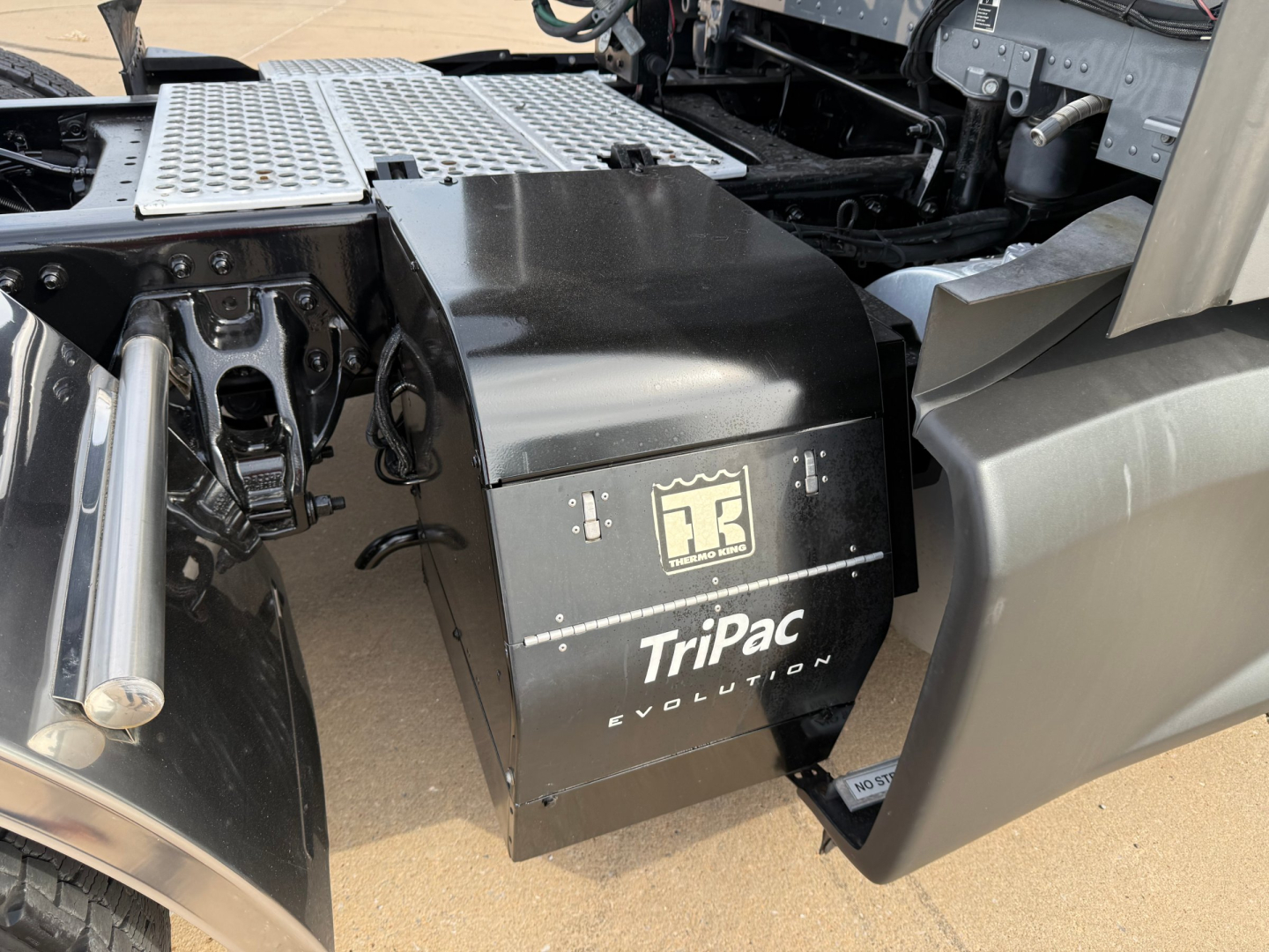 Kenworth T680 engine bay area showing Tripac Evolution battery/auxiliary power unit housing and metal steps.