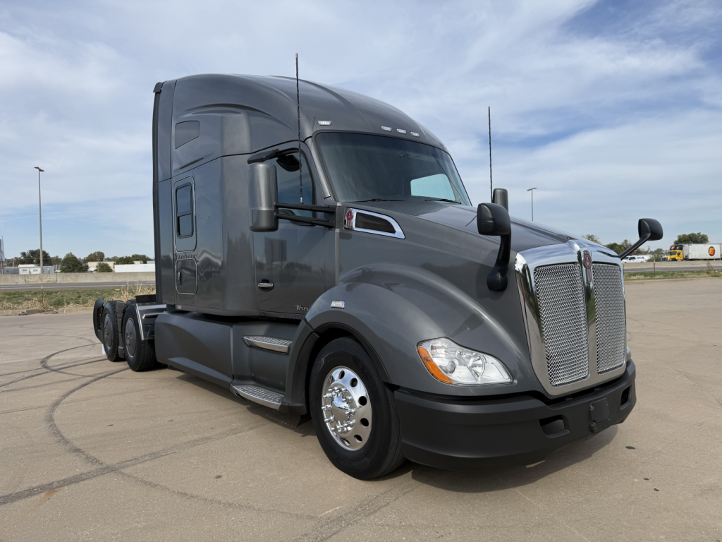 Kenworth T680 tractor-trailer cab in a dark gray color, forward view, showing front grille, headlights, large side mirrors, and sleeper cab with aerodynamic styling.