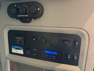 Kenworth T680 dashboard/console area showing climate controls, radio, and small controls in a sleeper cab. Thermo King unit visible above with circular knobs and a blue display on the radio.