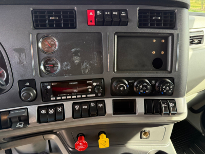 Kenworth T680 dashboard/controls showing gauges, switches, and climate controls; switches along bottom, knob dials, and a blank panel on the right.
