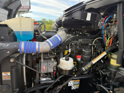 Kenworth T680 engine bay showing air intake hose, coolant reservoir, brake fluid reservoir, various hoses and wiring harnesses.