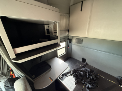 Kenworth T680 sleeper cab interior showing storage compartments and seating area with upper bunk folded and side paneling.