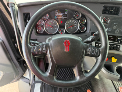 Steering wheel and instrument cluster inside a Kenworth T680 cabin showing gauges and controls.