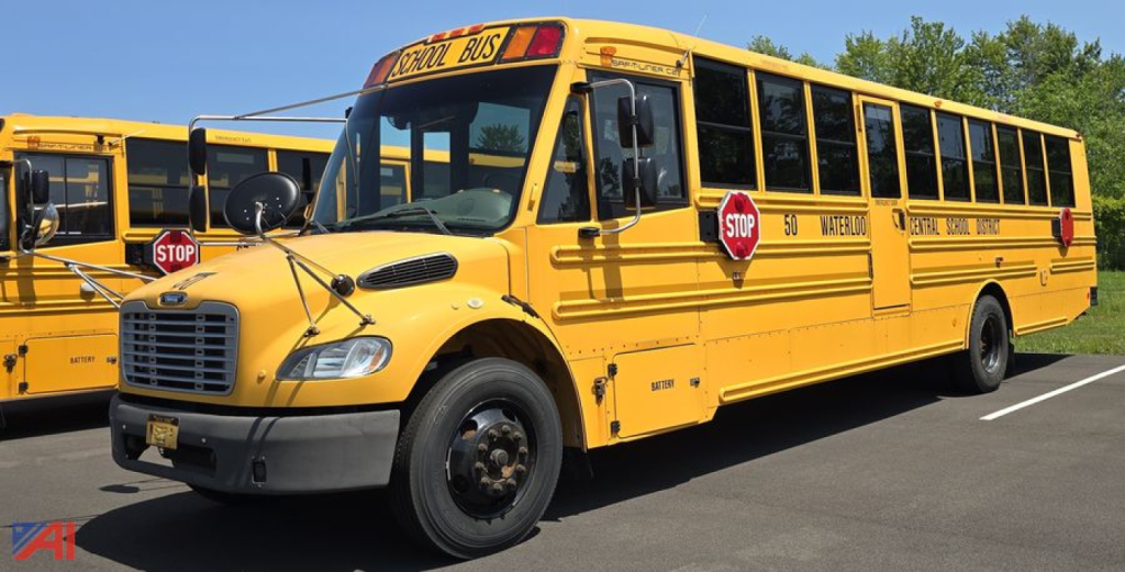 School bus with wheelchair lift in yellow showing Stop signs and side lettering, front grille, and windshield; Freightliner Thomas B2B C2 model; parking lot.