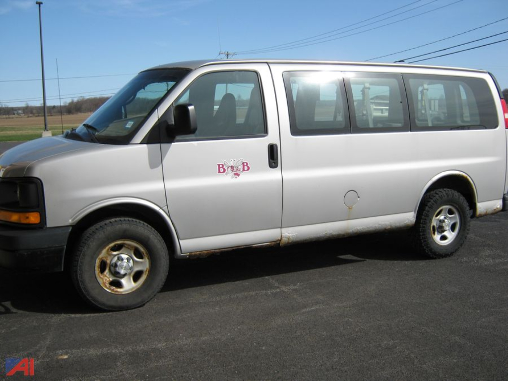Chevrolet Express 1500 cargo van side view showing passenger windows and purple B-side logo, with a wheel and minor body rust near bottom.