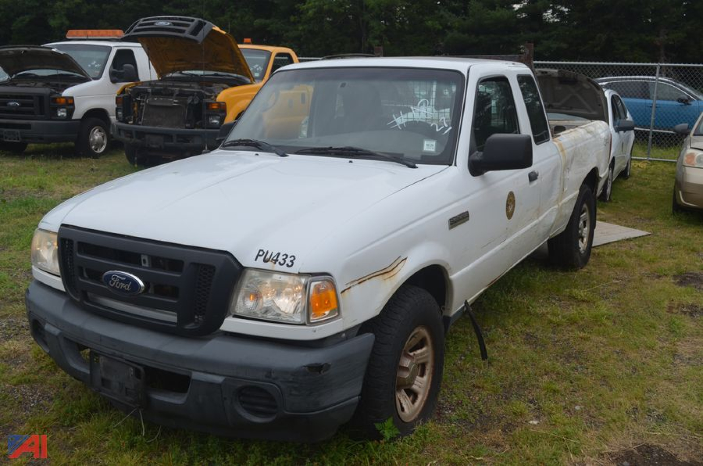 2011 Ford Ranger extended cab pickup truck in white, front left view, with damaged bumper and rust spots, side badge visible, utility yard background.