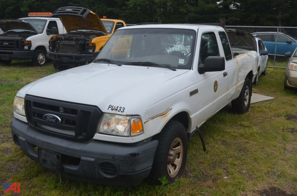 2011 Ford Ranger extended cab pickup truck in white, front left view, with damaged bumper and rust spots, side badge visible, utility yard background.