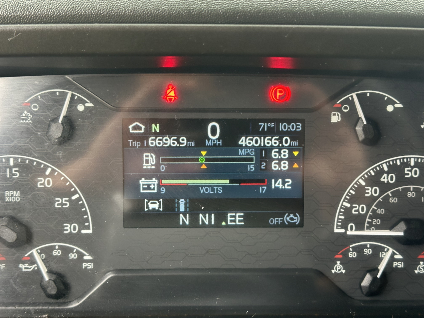 Dashboard of a 2021 Volvo VNL64T760 showing digital display with trip mileage 6696.9 mi, odometer 460166.0 mi, fuel, volts, and gear indicator in N. Visible icons: parking brake, seat belt warning, time 10:03, outside temp 71°F.
