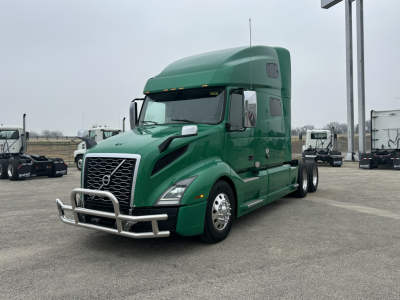 Green 2021 Volvo VNL64T760 sleeper tractor in a parking lot, front three-quarter view, with chrome bumper guard and grille.