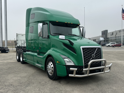 Volvo VNL64T760 sleeper tractor in green, front-left view showing chrome grille, bumper guard, and side mirrors.