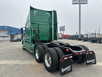 Truck rear and cab of a green Volvo VNL64T760 tractor. Twin rear axles, fifth wheel area visible, mud flaps with Bruchners logo, truck yard in background.
