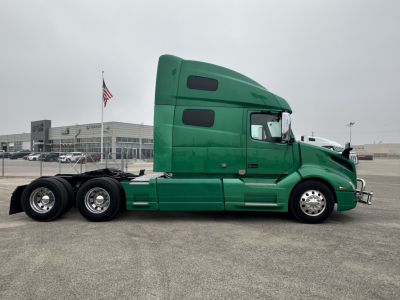 Green Volvo VNL64T760 sleeper cab truck side view showing chrome wheels and dual rear axles.