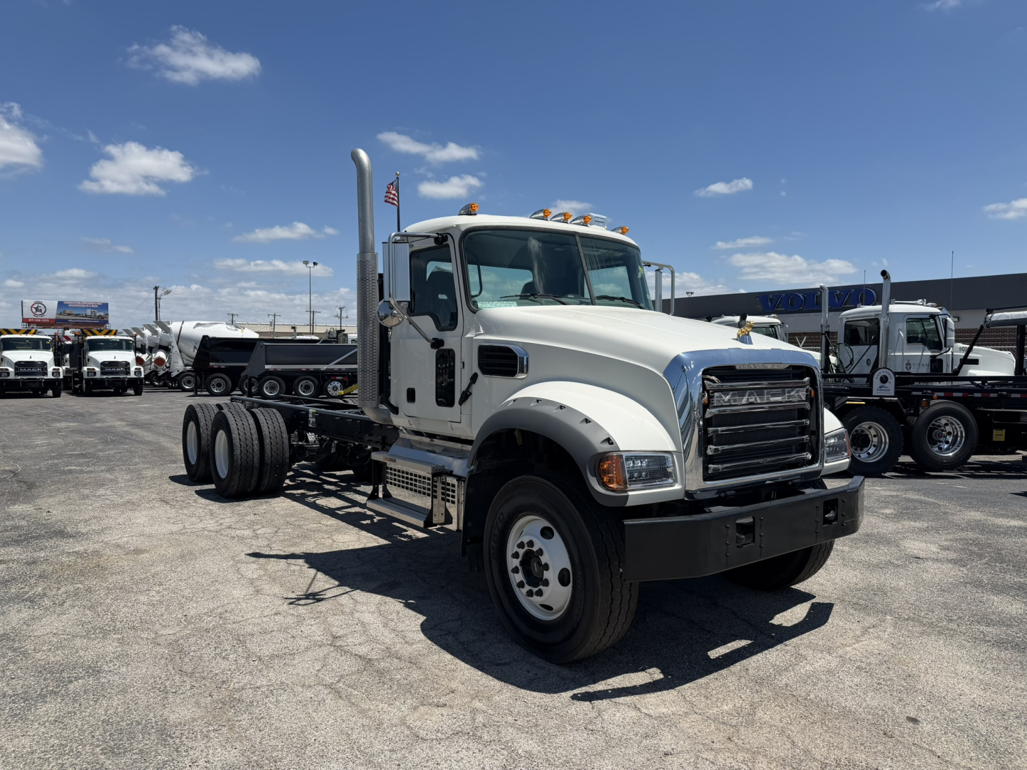 Front-left view of a white 2025 Mack GR64F cab and chassis truck with dual rear axles and chrome grille, parked in a dealership lot.