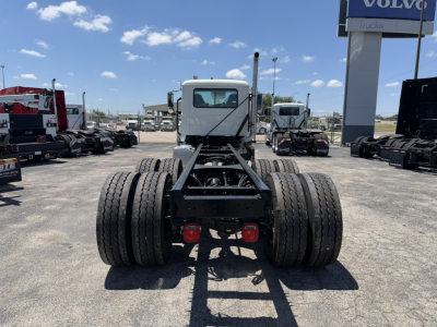 Rear view of a 2025 Mack GR64F cab and chassis showing dual rear axles with eight tires, chassis frame, cab in white, clear blue sky.