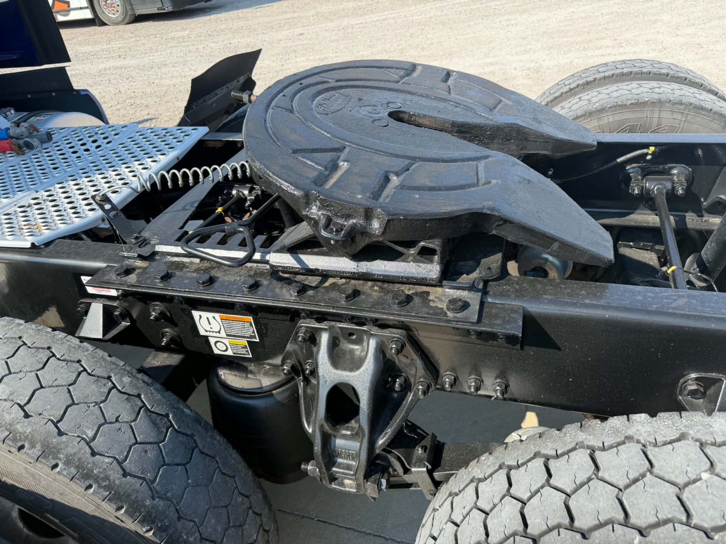 Kenworth T680 truck chassis with rear platform and mounted spare wheel; visible components include a circular fifth-wheel/line for towing, coil springs, black metal frame, and a warning label on the side.