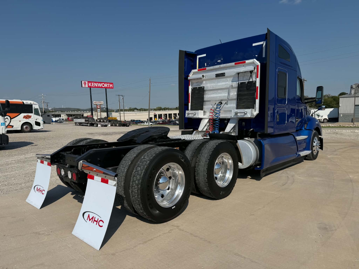 Kenworth T680 tractor rear view showing dual rear axles and fifth wheel, chrome fuel tanks, and blue sleeper cab with rear equipment.