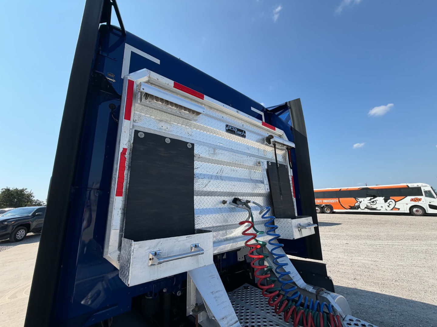 Kenworth T680 dump truck rear showing chrome toolbox compartments, flexible red and blue air lines, and raised bed with metal panels.