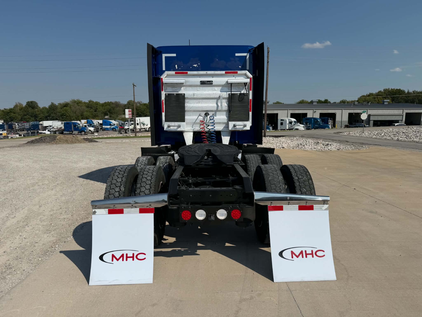 Kenworth T680 rear view showing fifth wheel, fuel tanks, and dual rear axles with mud flaps and MHC logo.