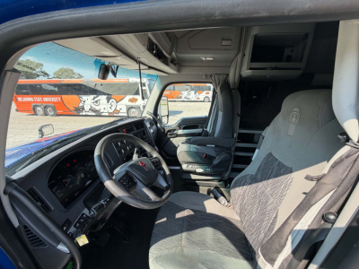 Kenworth T680 truck cab interior showing steering wheel, driver seat, and dashboard with overhead storage and a small monitor.