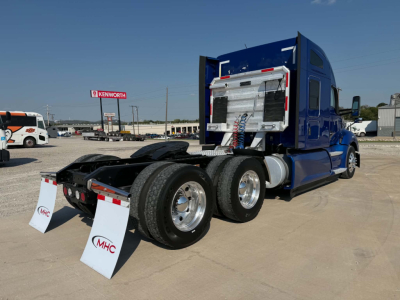 Kenworth T680 tractor rear view showing dual rear axles and fifth wheel, chrome fuel tanks, and blue sleeper cab with rear equipment.