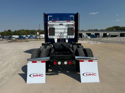 Kenworth T680 rear view showing fifth wheel, fuel tanks, and dual rear axles with mud flaps and MHC logo.
