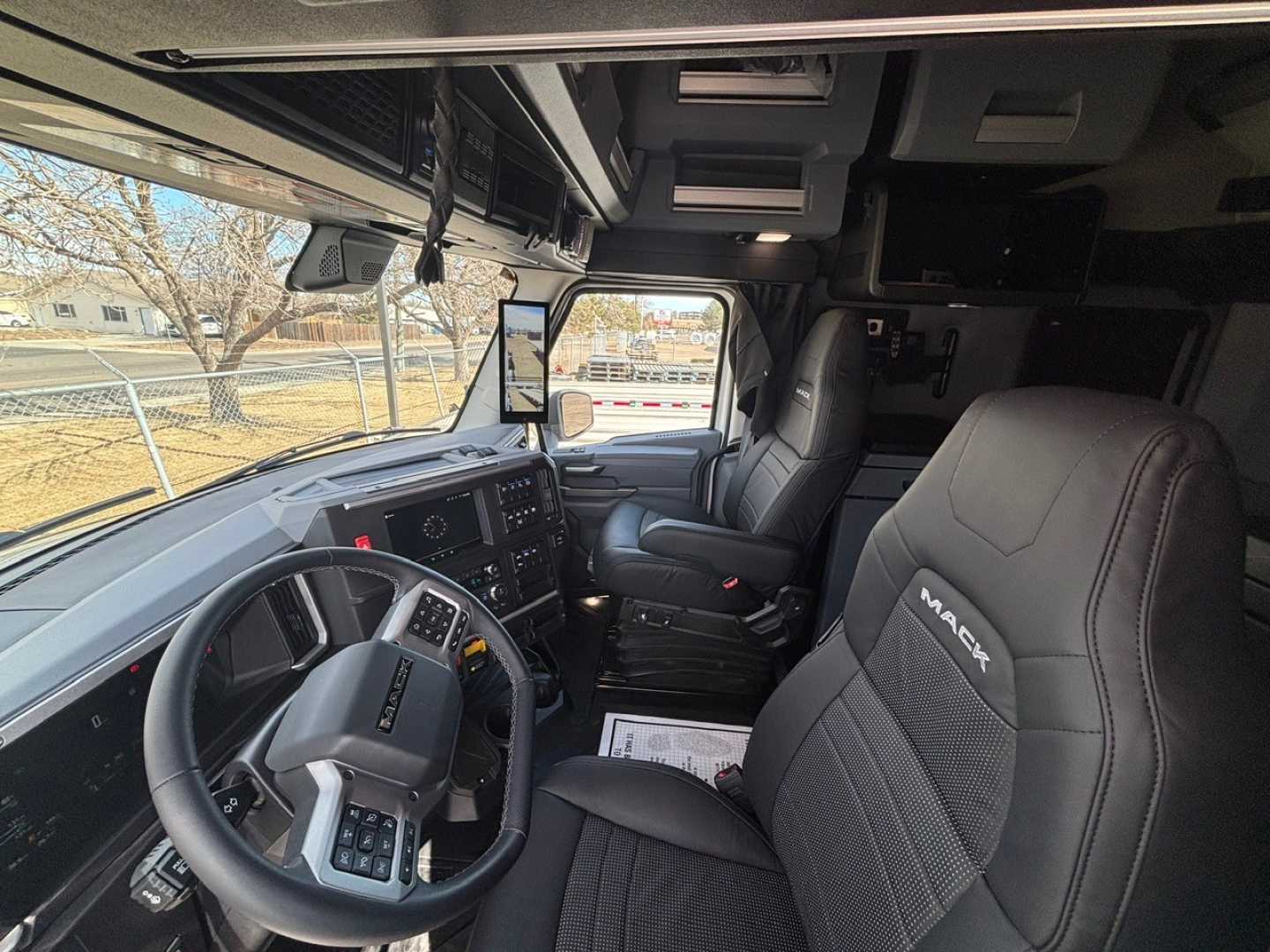 Cab interior of a 2026 Mack PR64T76M showing steering wheel, dash, and driver seat with Mack logo embroidered.
