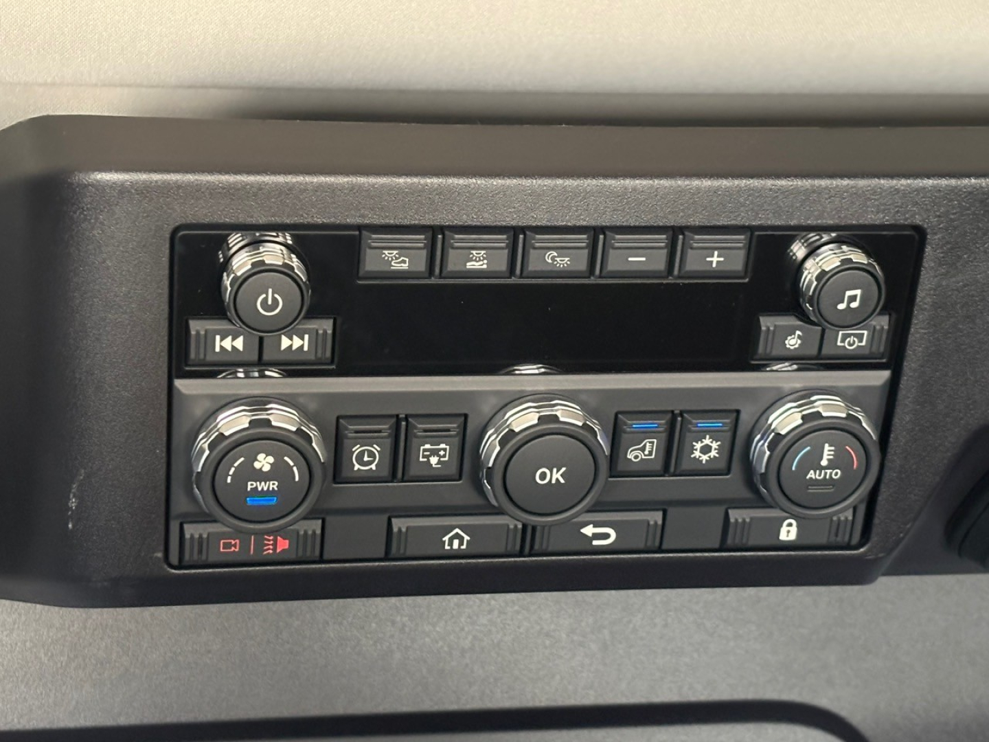 Dashboard controls panel with buttons and knobs in a Mack PR64T76M truck cab showing climate and media control interface.
