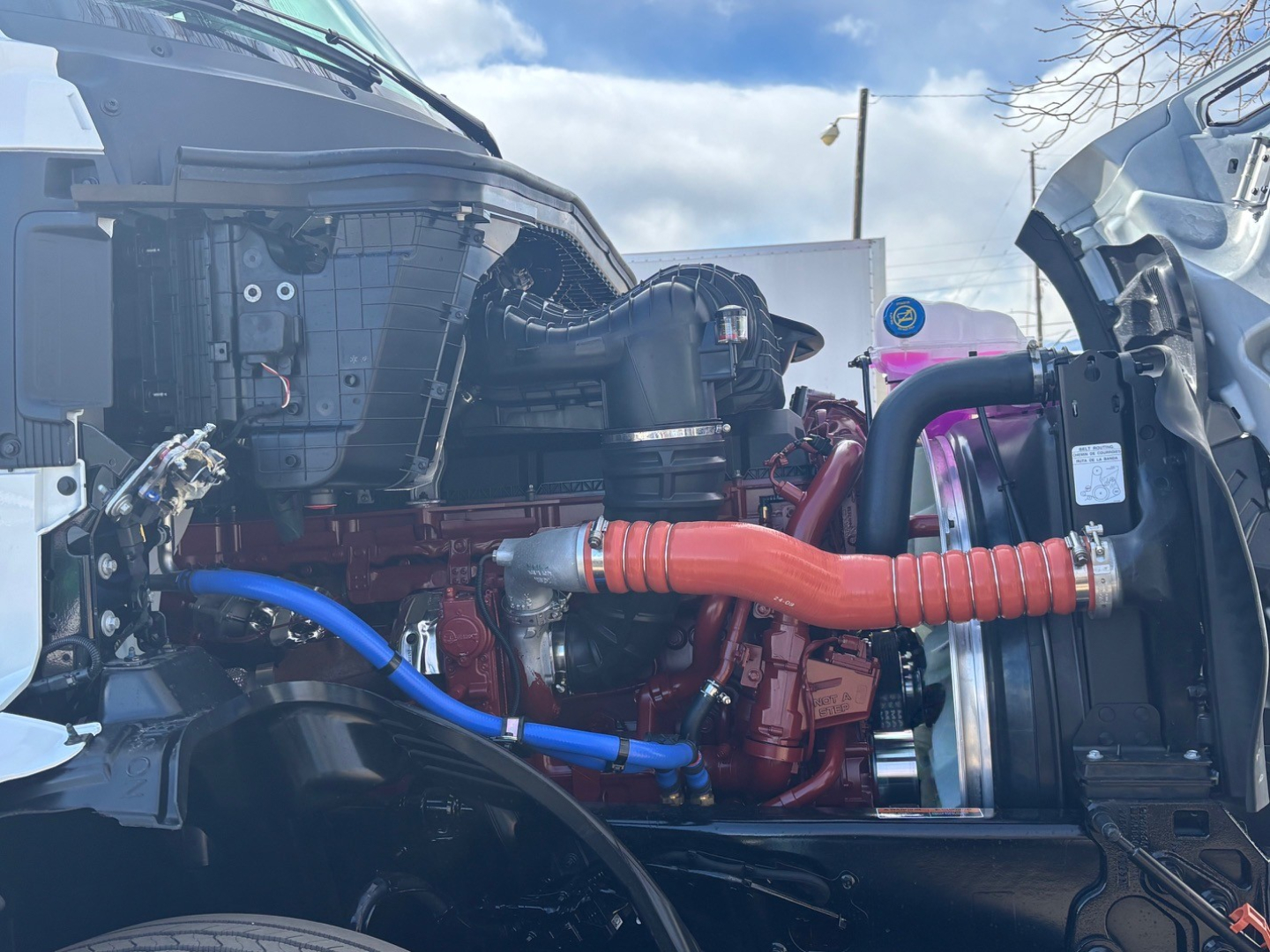 Mack PR64T76M engine bay showing red engine block, orange braided intercooler hose, blue coolant hose, and surrounding components.