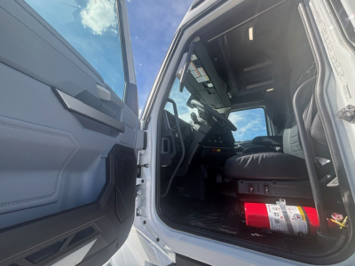Truck cab interior of a 2026 Mack PR64T76M showing driver seat and dashboard from open door with a fire extinguisher in the cab.