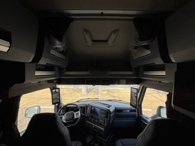 Cab interior of a new 2026 Mack PR64T76M sleeper truck showing dashboard, overhead bunk storage, and driver seat view.