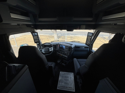 Interior of new Mack PR64T76M conventional sleeper cab showing dashboard, steering wheel, and two driver/passenger seats; large infotainment screens mounted on A-pillars.