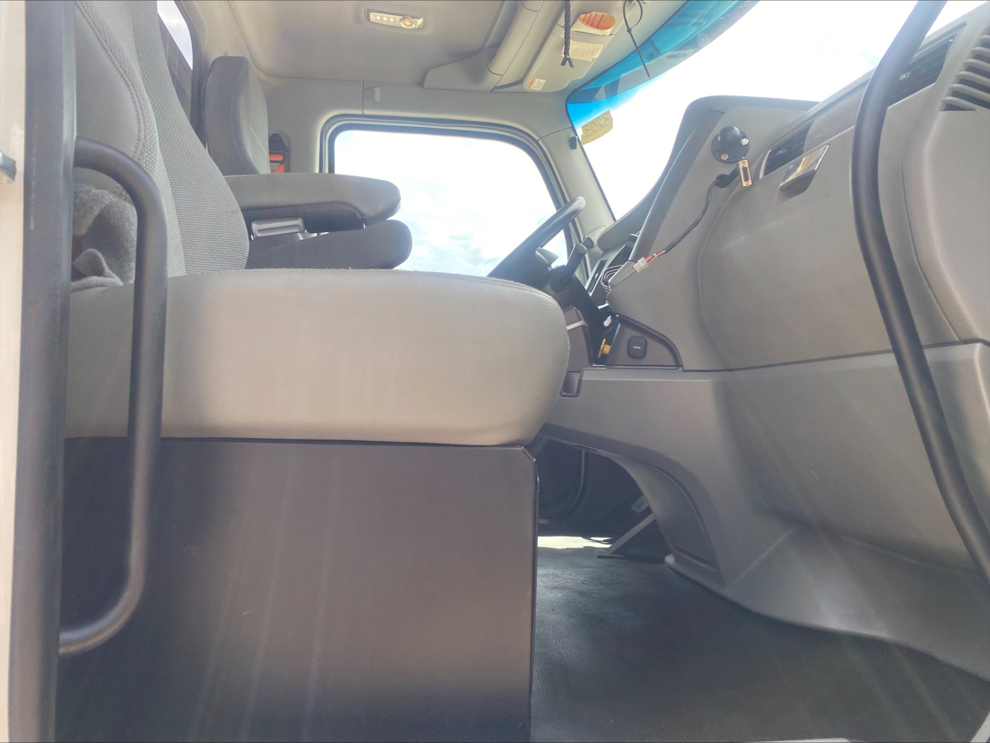 Kenworth T880 cab interior showing driver seat and dashboard with steering wheel, windshield, and pedals visible.