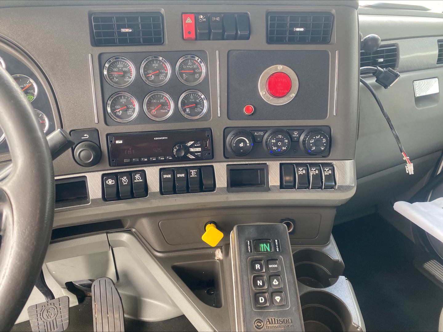 Kenworth T880 dashboard and center console showing gauges, control switches, red emergency button, and gear shifter with APU/air system controls.