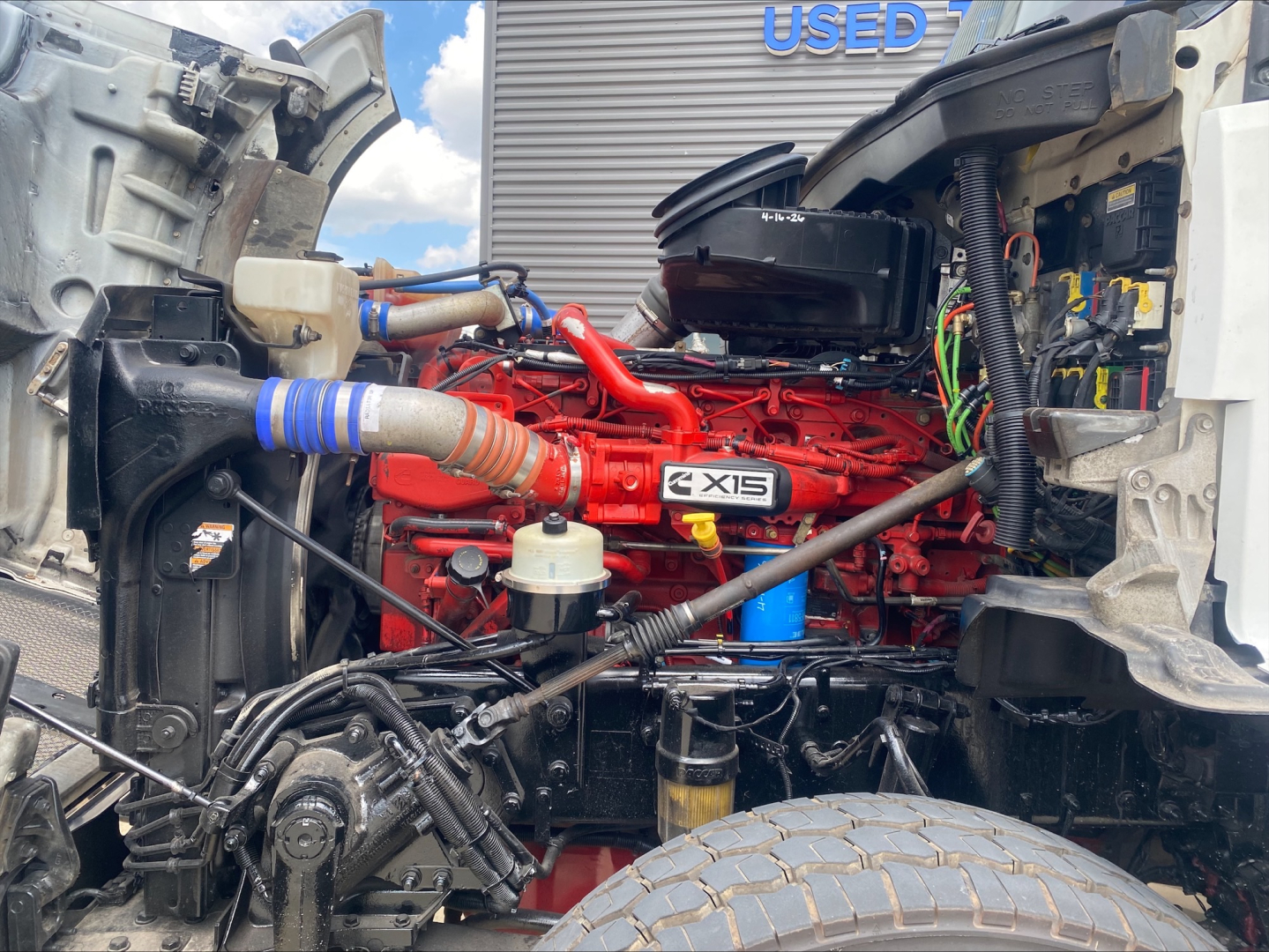 Kenworth T880 engine bay showing Cummins X15 engine with red block, air intake, hoses, wiring, and surrounding components.