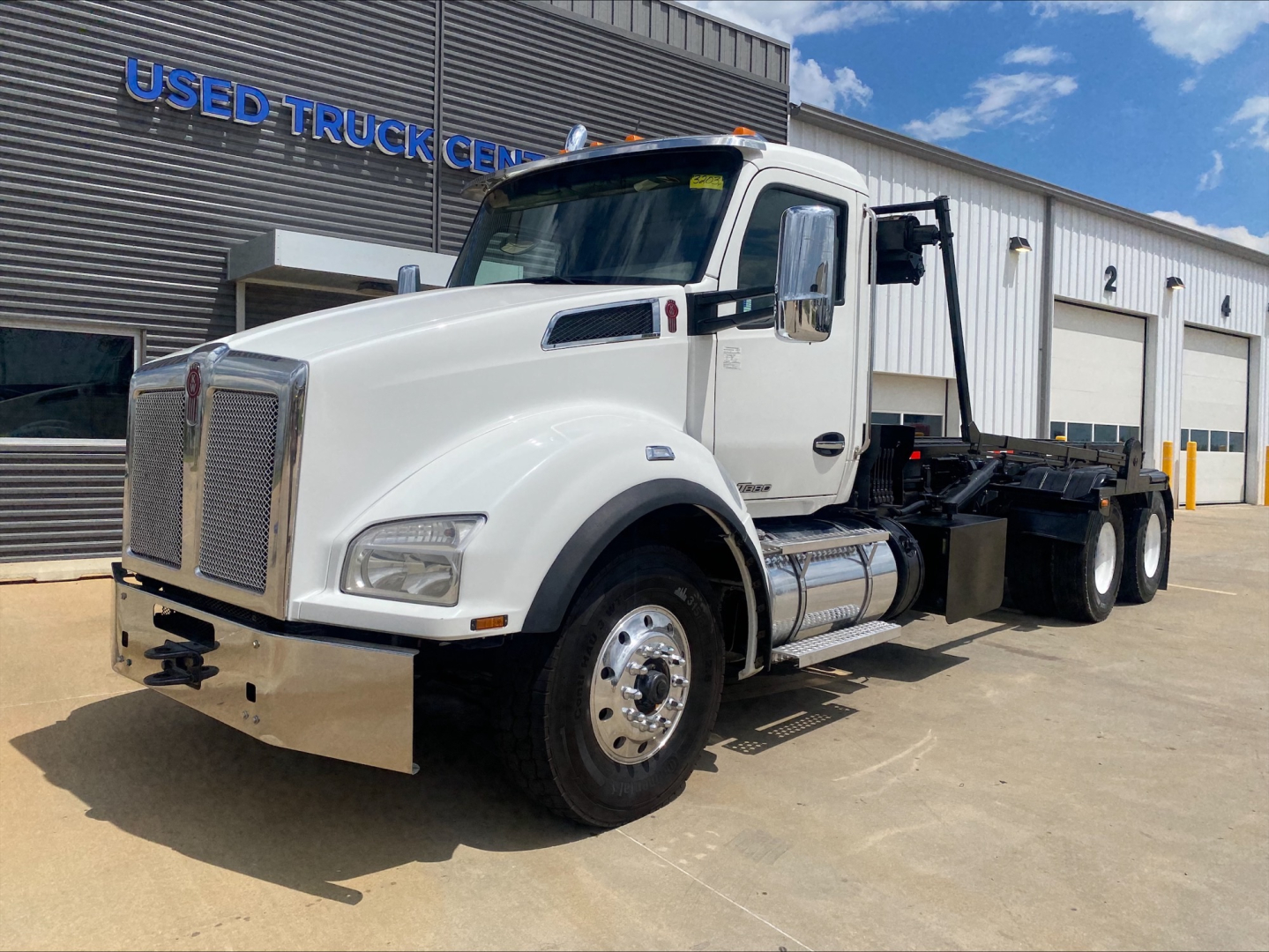 Kenworth T880 rolloff truck in white, front-side view showing cab, chrome bumper, and aluminum fuel tanks.