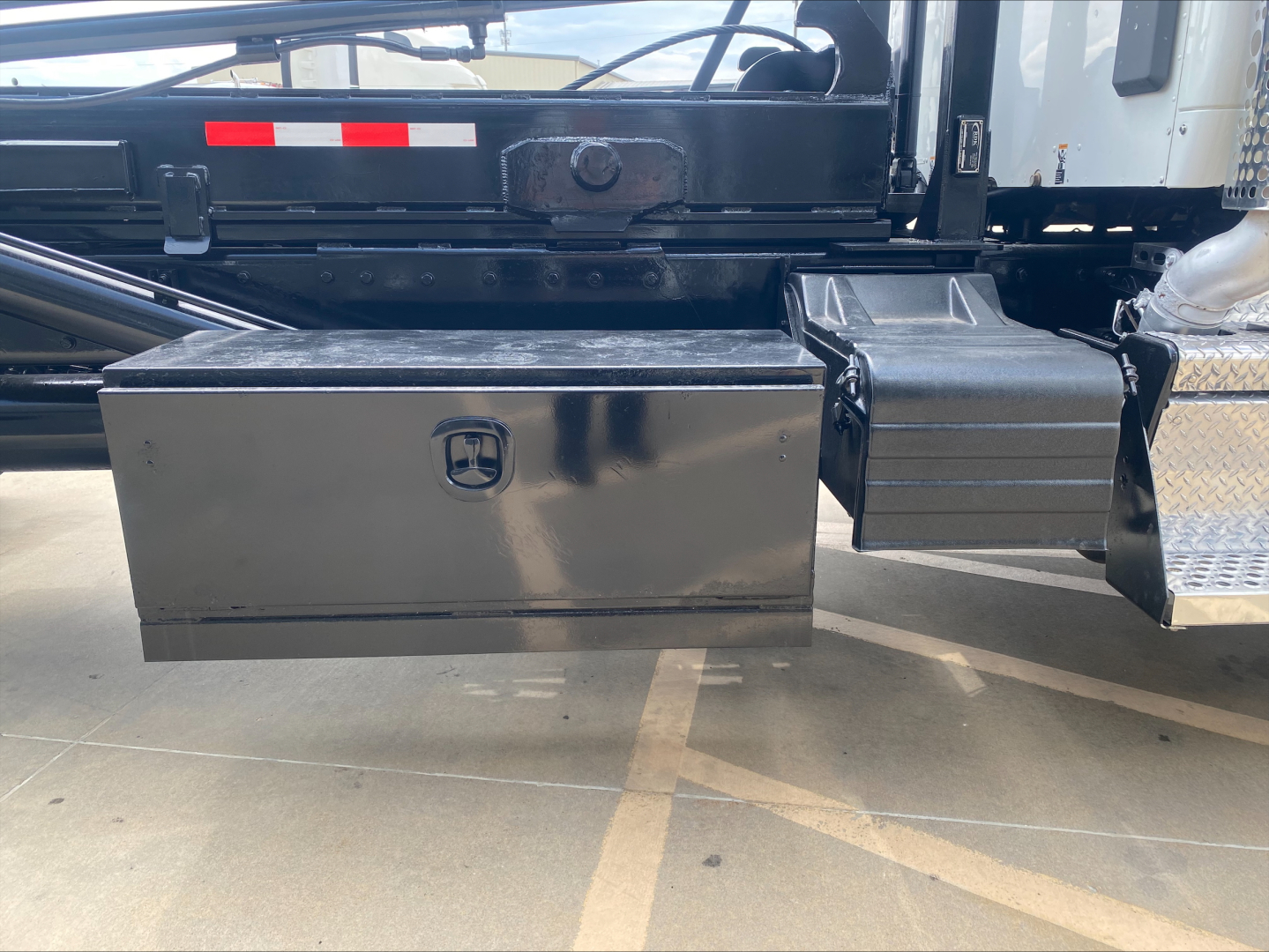 Kenworth T880 side view showing a black metal toolbox with a rounded logo and a step/side frame in the truck chassis.