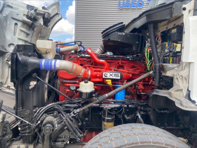 Kenworth T880 engine bay showing Cummins X15 engine with red block, air intake, hoses, wiring, and surrounding components.