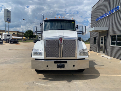 Kenworth T880 front view with badge grille and chrome bumper. Diesel exhaust stacks visible, yellow clearance lights on cab, dealership building in background.