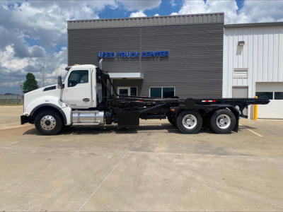 Kenworth T880 roll-off truck in front of a building, side view showing long chassis and multiple axles.